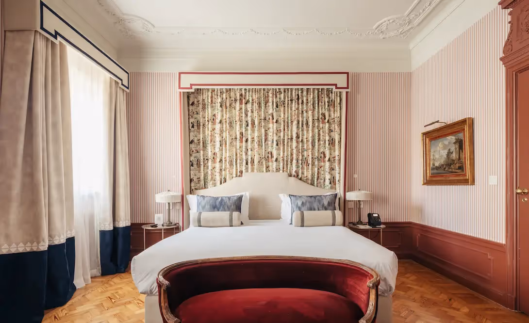 Elegant bedroom at Hotel Experimental Infante Sagres in Porto with a white bed, floral fabric alcove, and red velvet bench.