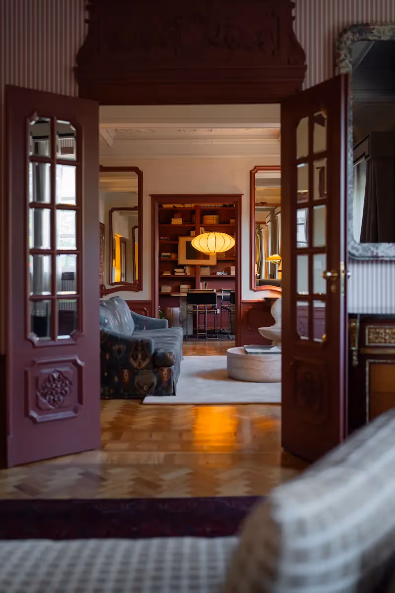 View through open burgundy doors into an elegant lounge with herringbone parquet at the Hotel Experimental Infante Sagres in Porto.