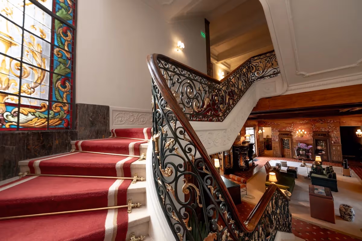 Monumental marble staircase with a red carpet and artistic stained glass at Hotel Experimental Infante Sagres in Porto.