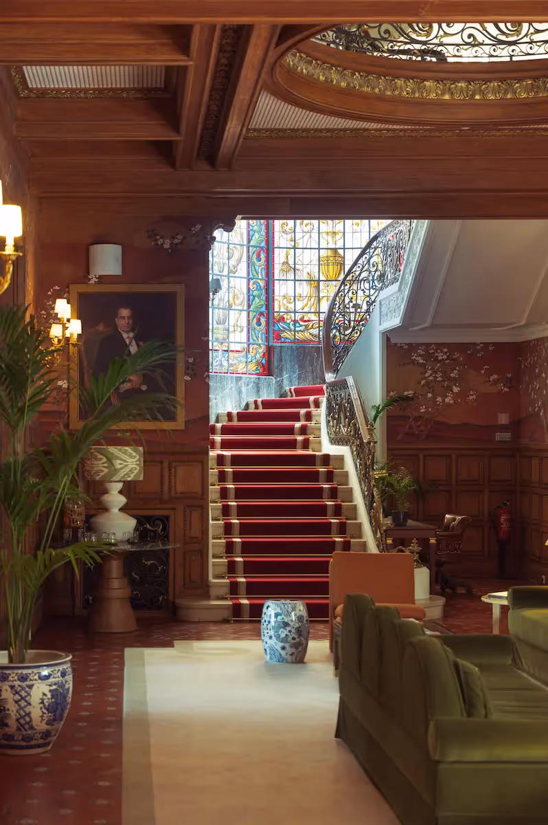 Monumental marble staircase with a red carpet and artistic stained glass at Hotel Experimental Infante Sagres in Porto.