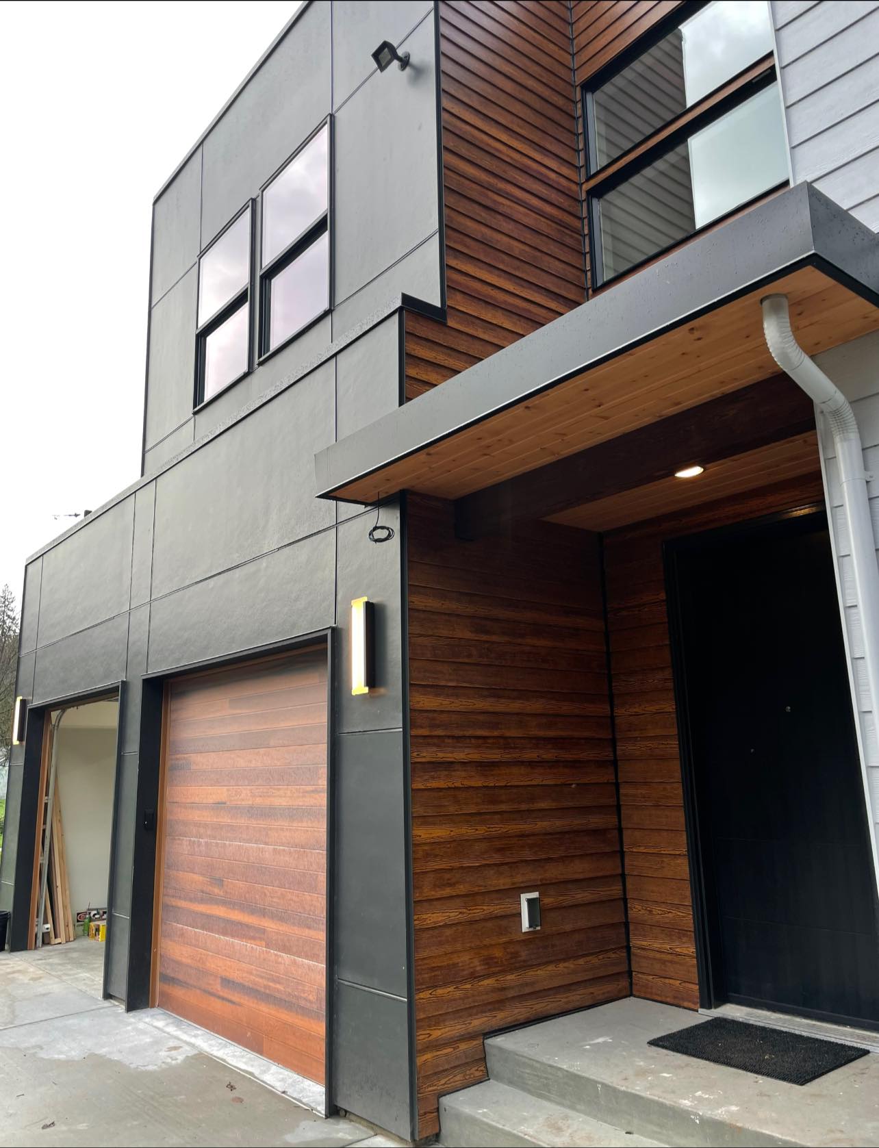 Completed modern home build with wood siding, metal panels, and custom garage door
