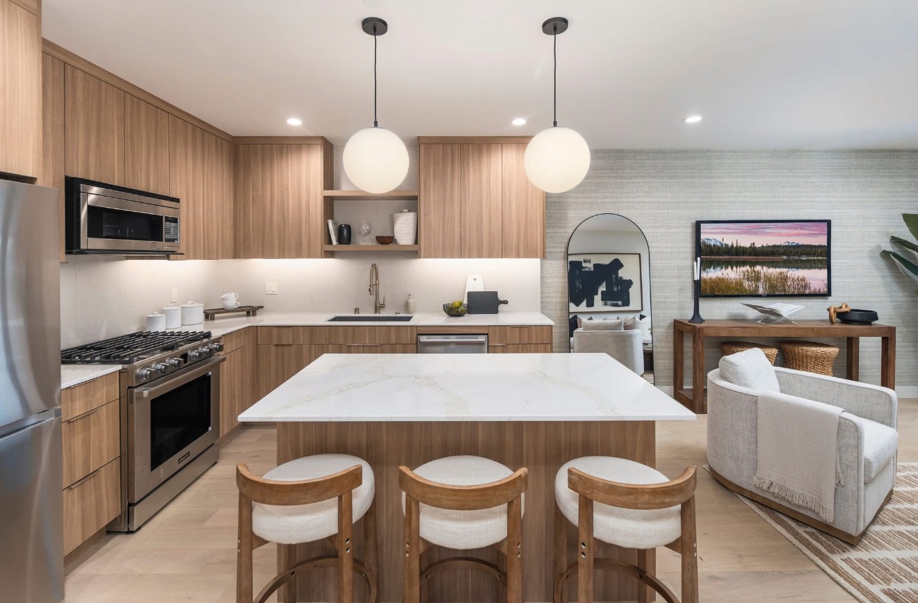 Modern kitchen featuring flat-panel wood cabinets, quartz island with seating, globe pendant lights, and integrated appliances in an open living space