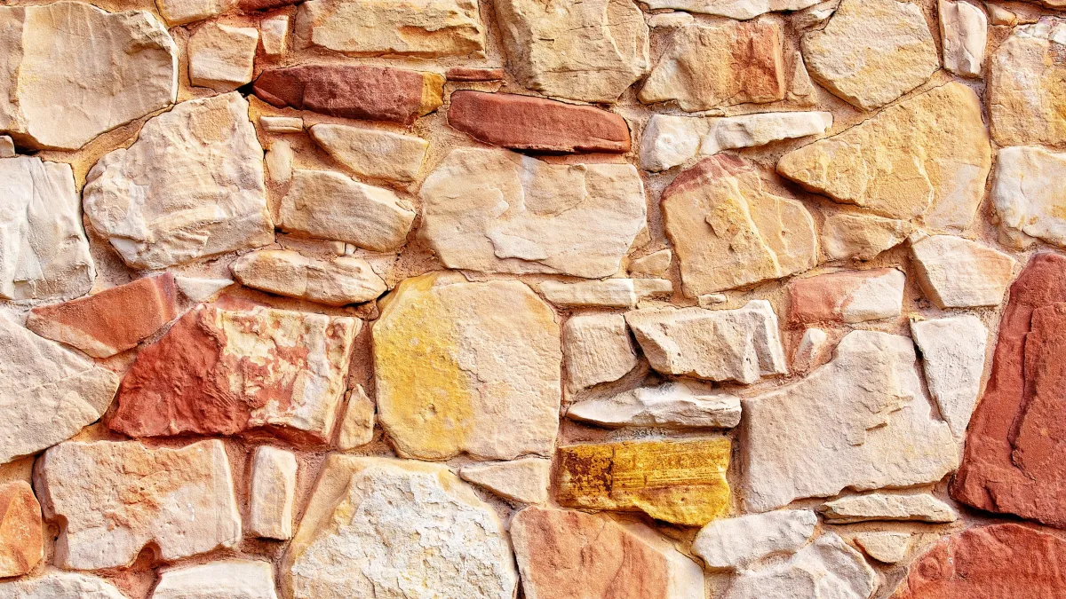 Monivärisistä oranssin, keltaisen ja beigen sävyistä kivistä rakennettu tiiliseinä.