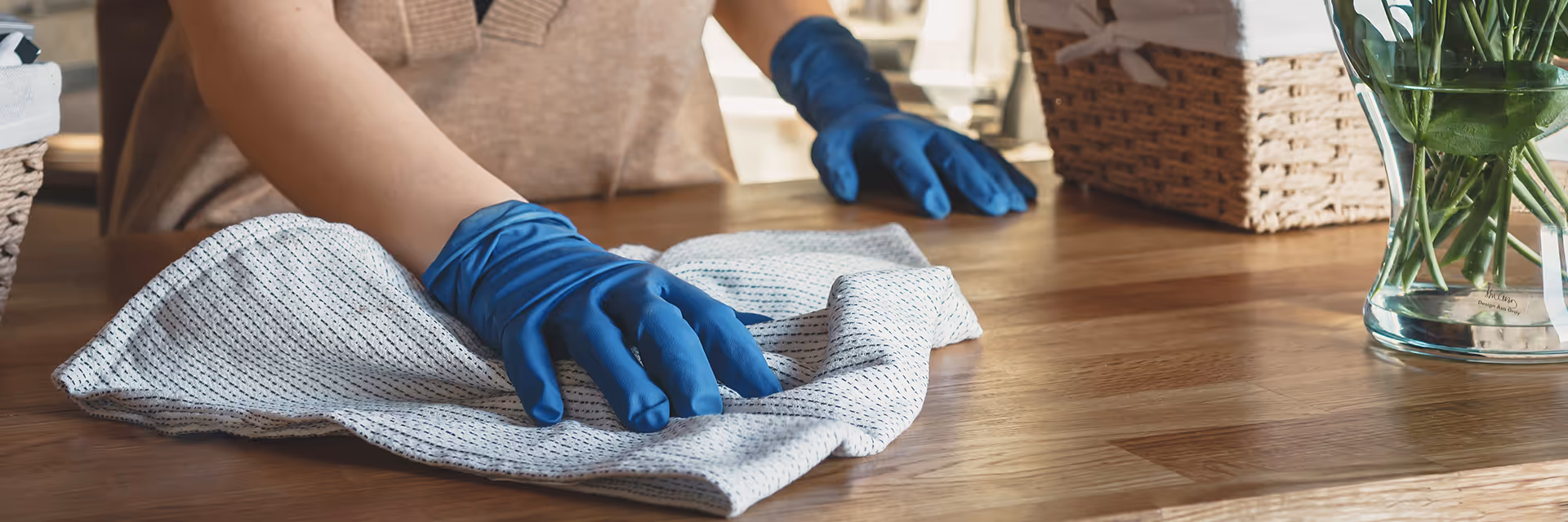 Hemma-avustaja pyyhkii puupöytää  suojakäsineissä liinalla.