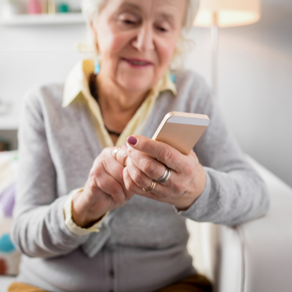 Iäkäs nainen käyttää älypuhelinta sohvalla istuen.