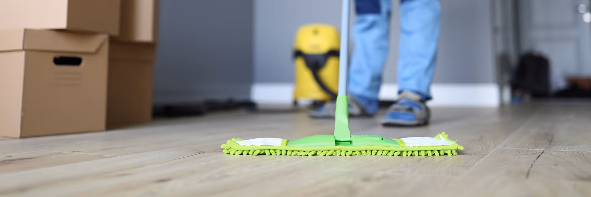 Hemma-avustaja pyyhkii lattiaa vihreällä mikrokuitumopilla puuparkettilattialla.