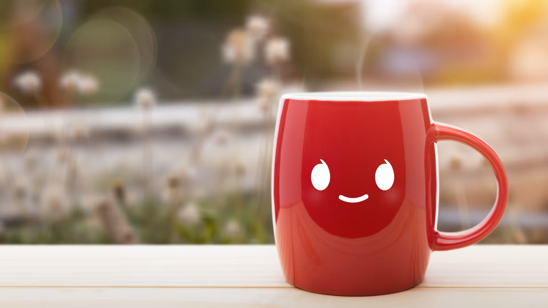 Punainen kahvimuki, jossa on hymyilevä kasvokuvio, puupöydällä ulkona sumuisessa taustassa.