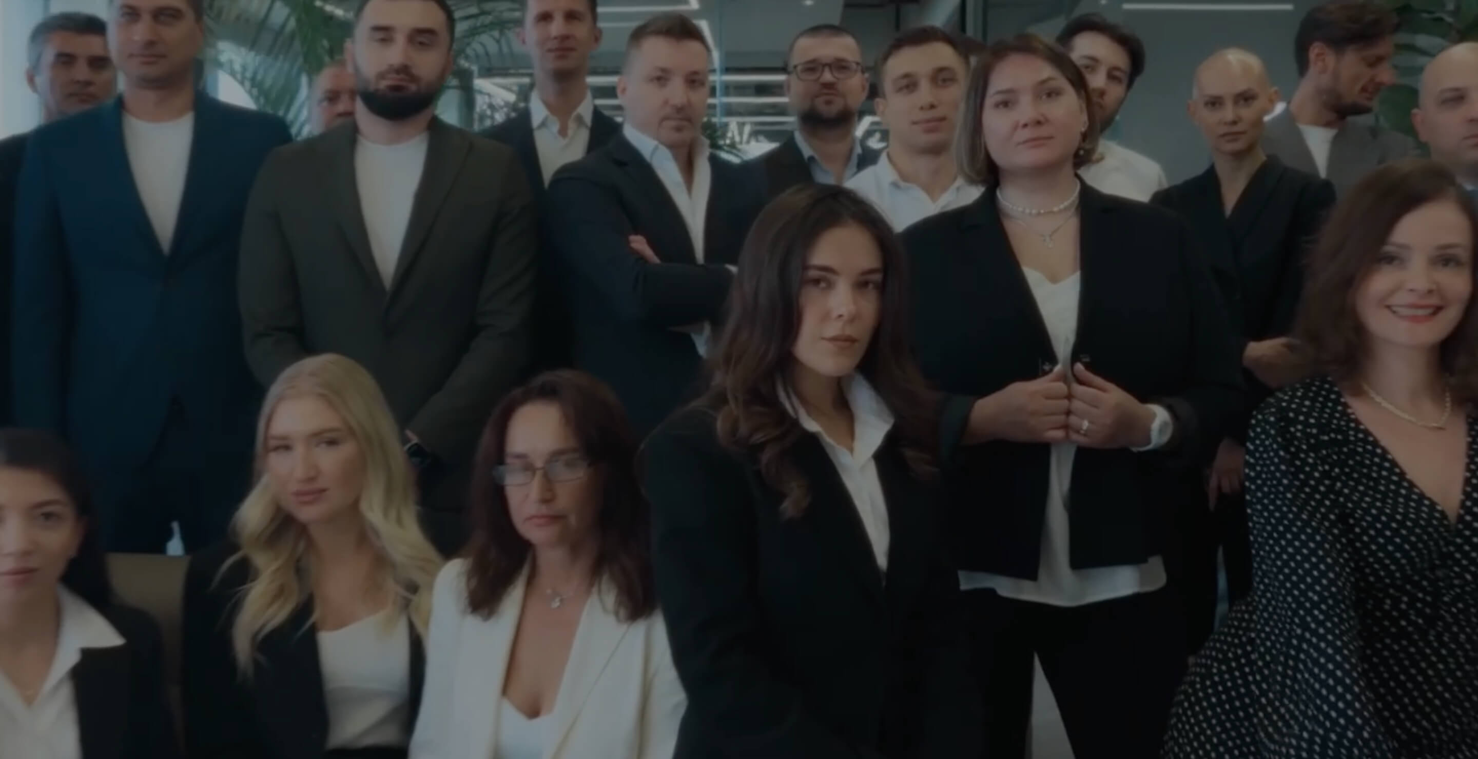 Group of professionally dressed men and women standing and sitting indoors, posing for a formal photo.