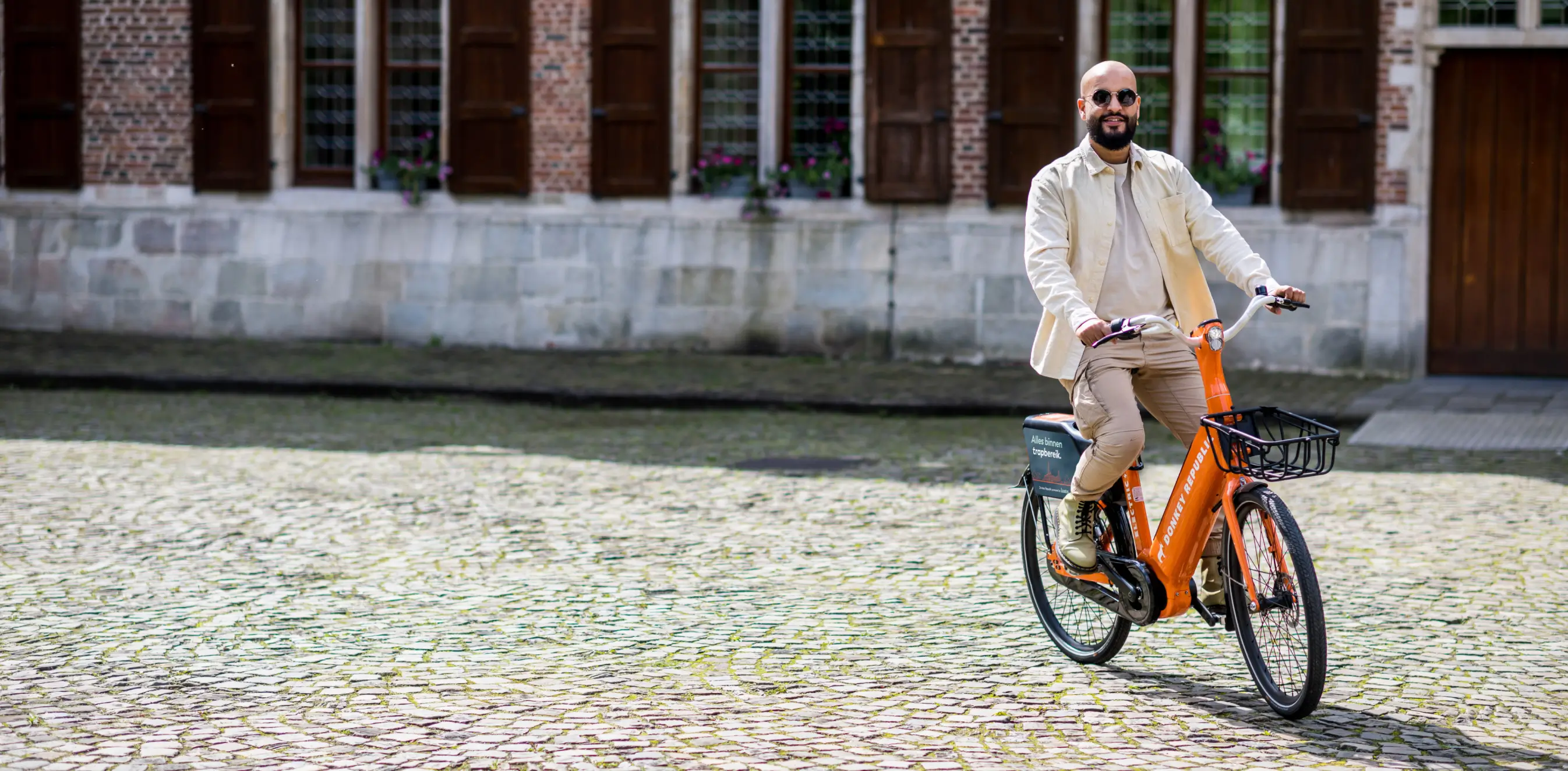 A man riding an orange bike down a cobblestone street.