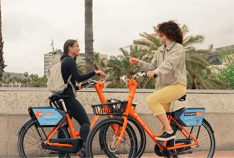 two women talking while riding orange bikes