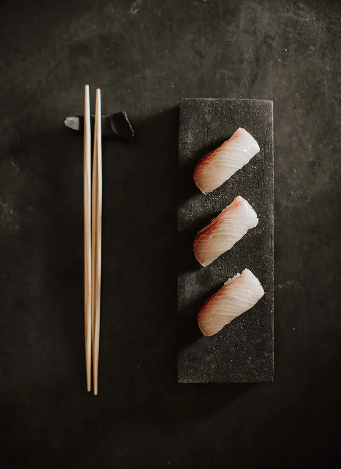 A display of three identical Sushi pieces, with chopsticks perfectly lined up next to the plate.