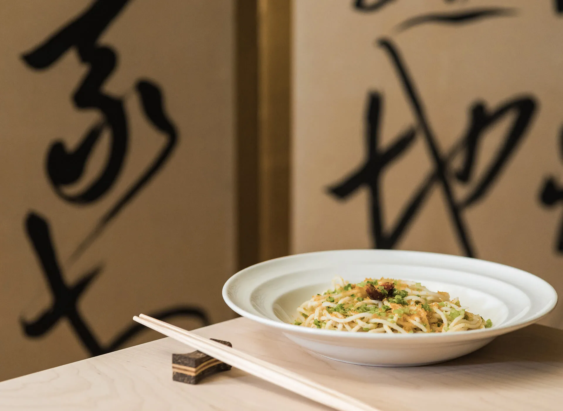 A bowl of noodles on a table, with Masa wall hangings in the background.
