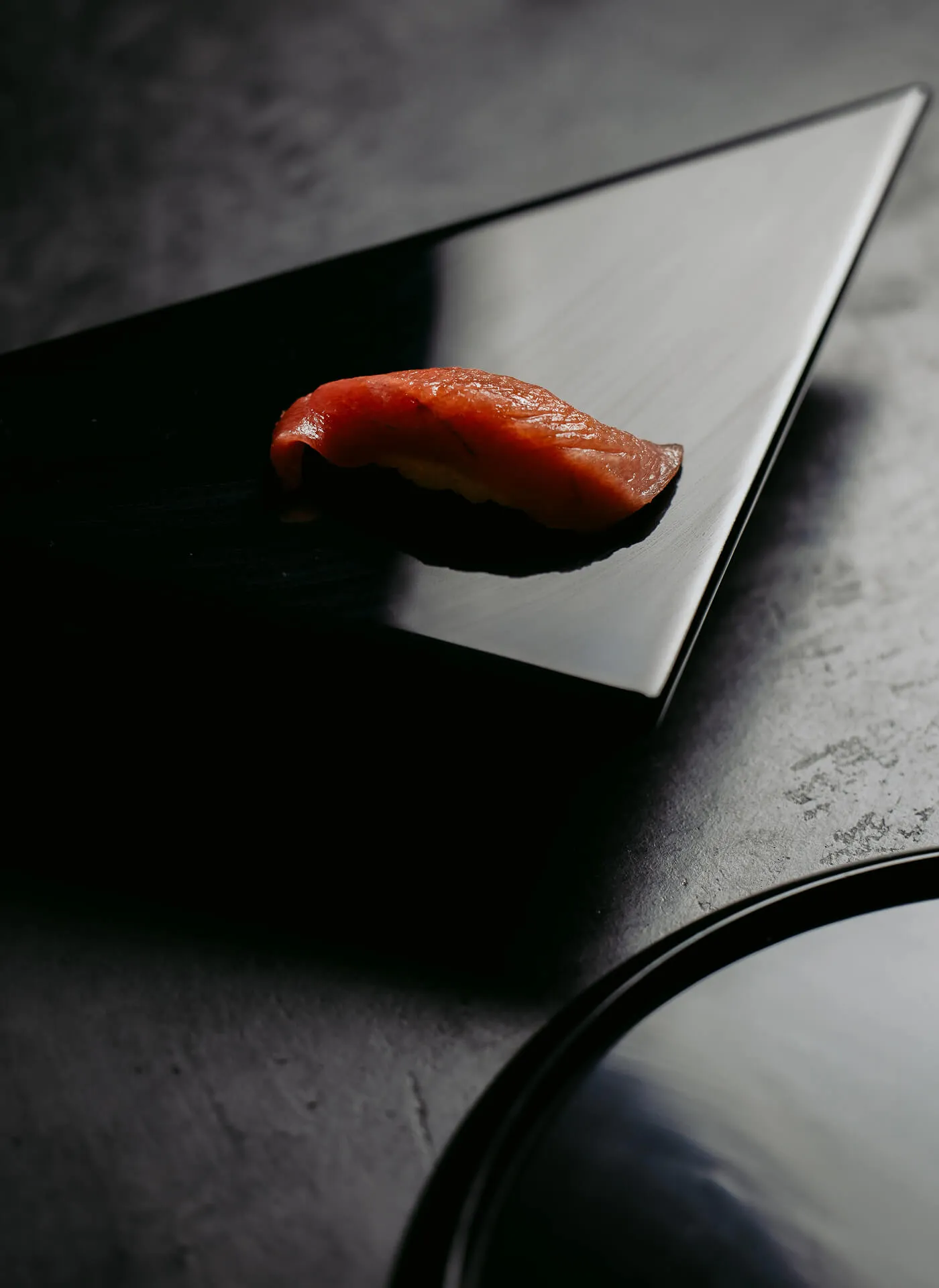 A singular pice of Sushi on a shiny black triangle plate