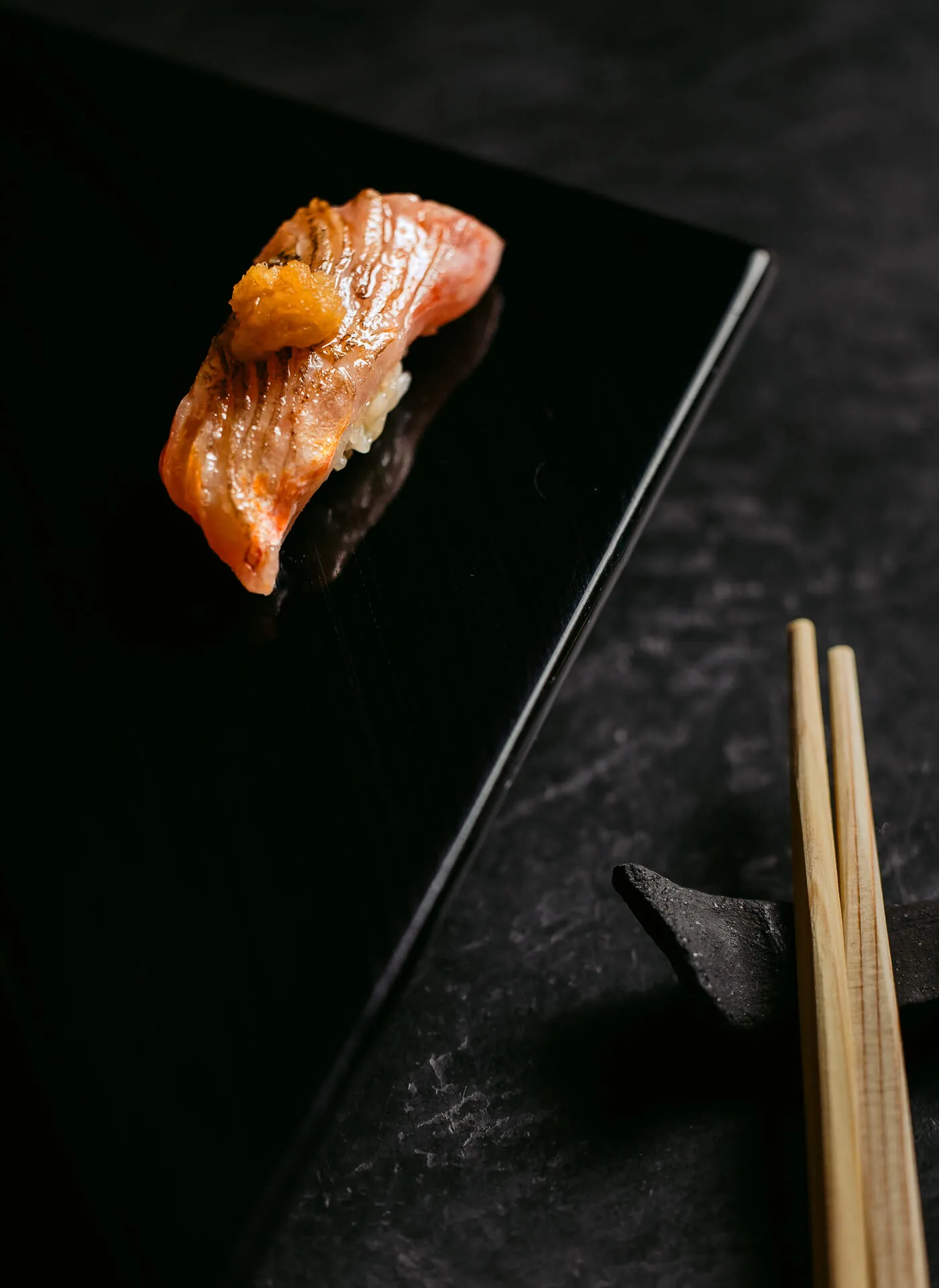A singular piece of sushi, with chopsticks carefully placed next to the dish.