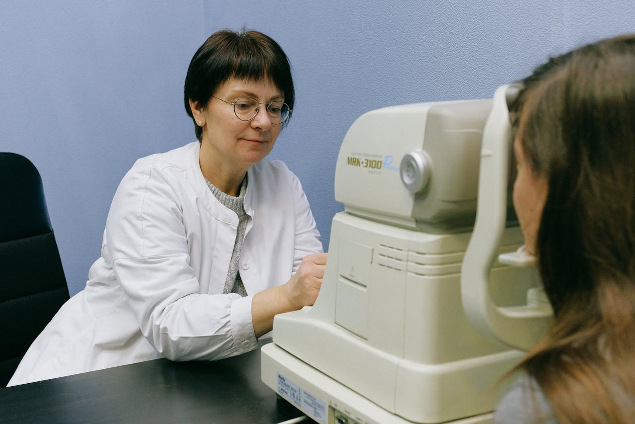 Female ophthalmologist wearing a white coat using an eye examination machine with a patient.