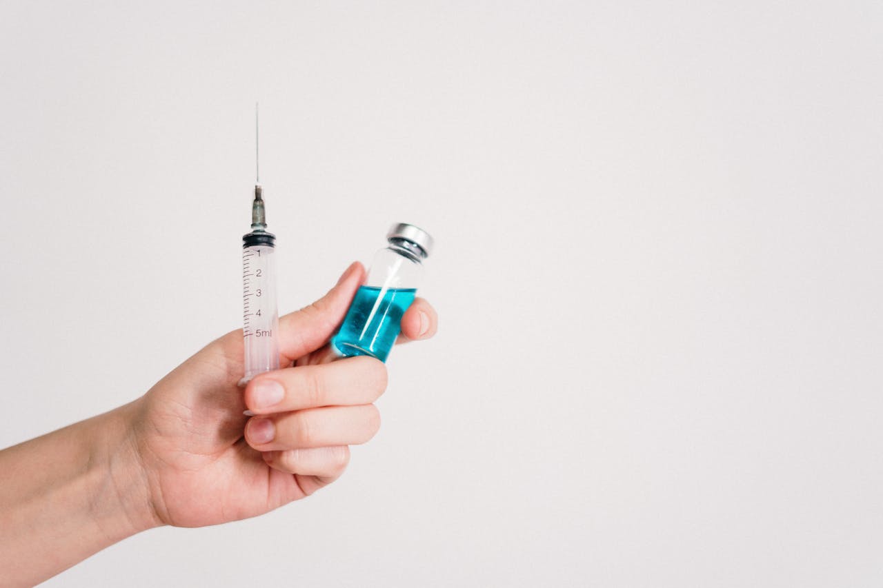 Hand holding a syringe and a small vial with blue liquid against a plain white background.