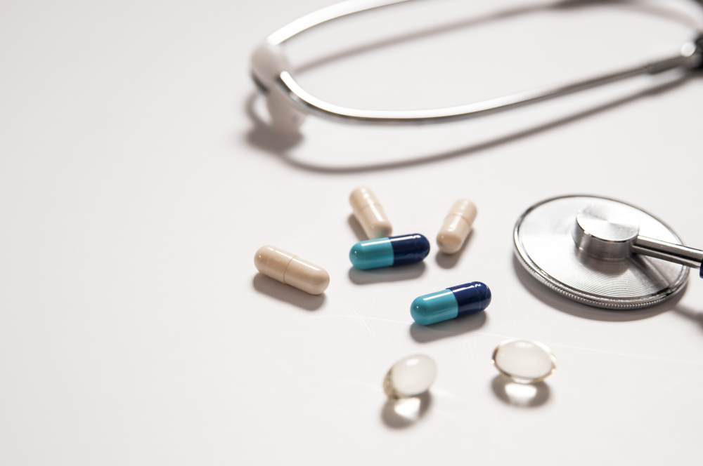 Beige capsules, blue and teal capsules, and transparent gel pills near a stethoscope on a white surface.