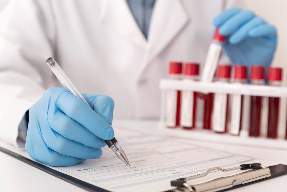 Person wearing blue gloves filling out a form with test tubes filled with blood in the background.