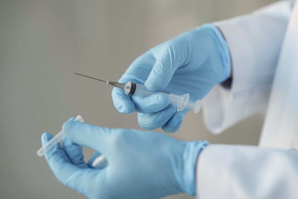 Hands in blue gloves holding a syringe with a needle and a vial cap.