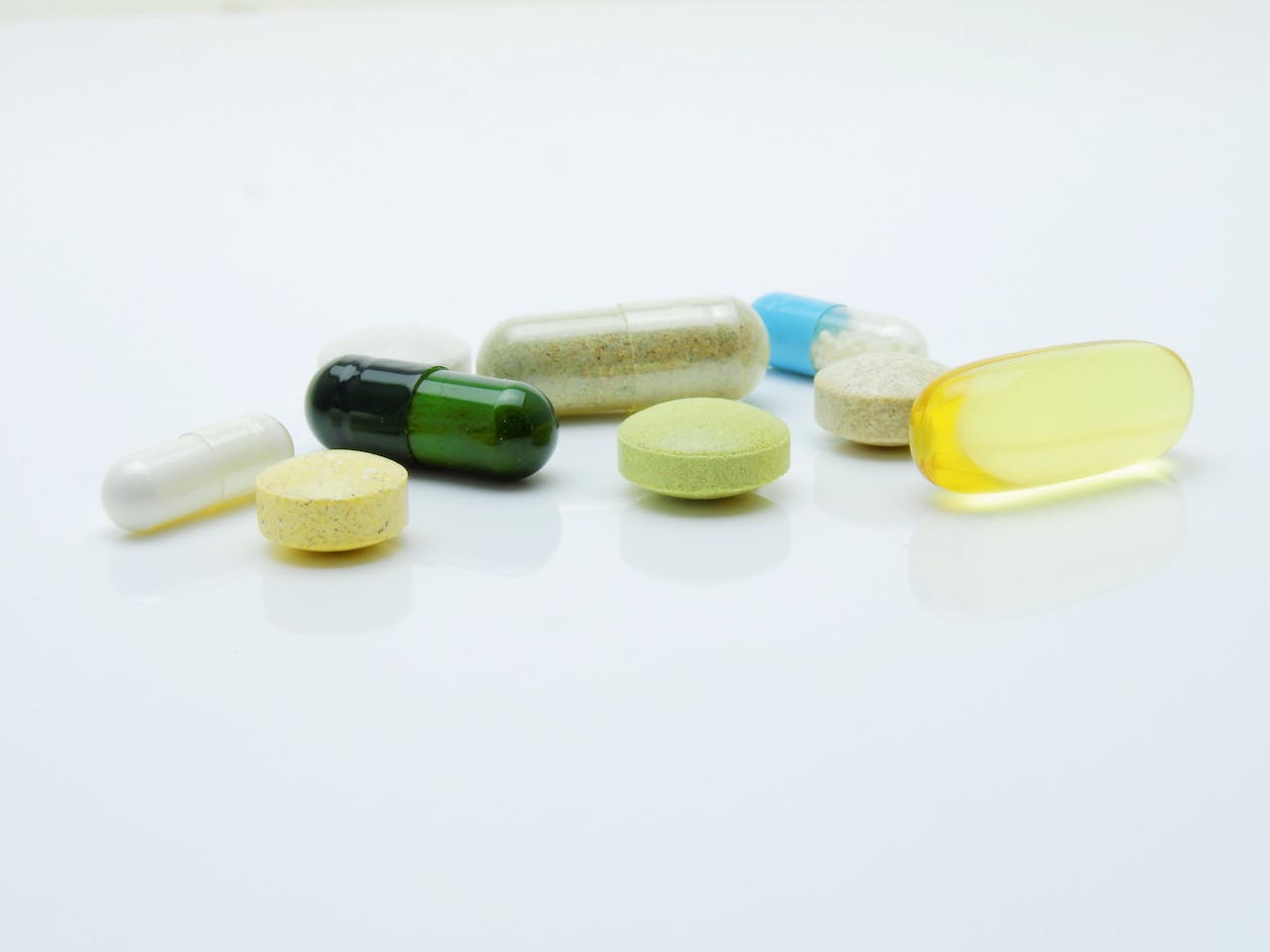 Assorted capsules and tablets in various colors and shapes on a white surface.