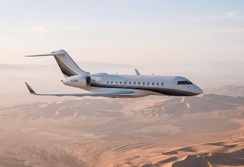 White private jet flying over desert dunes at sunset.