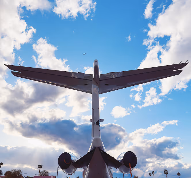 View from below of a large airplane with wings spread against a partly cloudy blue sky and a smaller plane flying in the distance.
