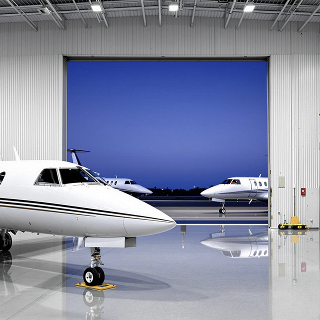 Dunes Air three white private jets parked near and inside a large hangar at dusk with clear blue sky.