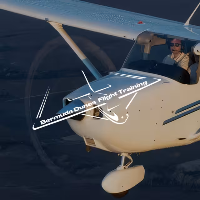 Small white airplane flying with two people inside, overlay graphic reads 'Bermuda Dunes Flight Training'.