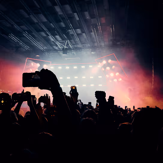 Crowd at a concert holding up phones and cameras with bright stage lights in the background.