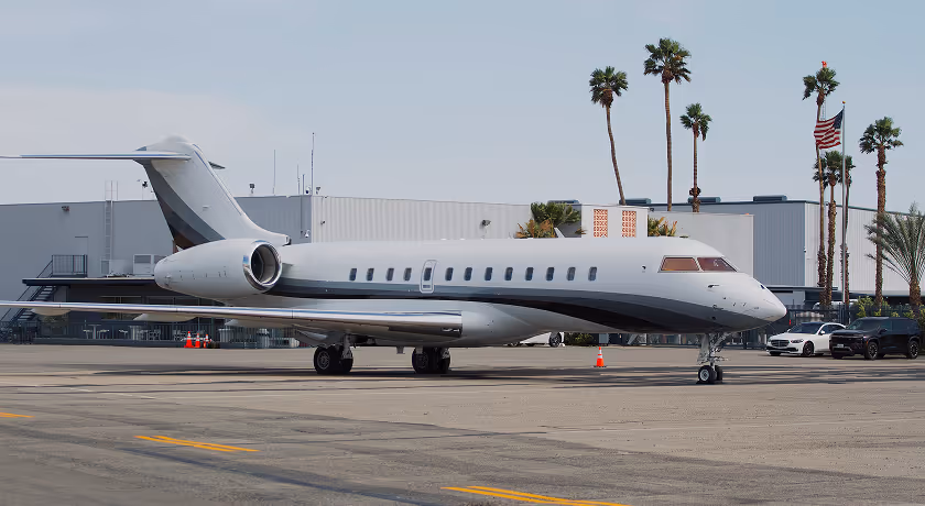 Dunes Air Runway with white private jet with gray and black accents parked on airport tarmac with palm trees and American flag in the background.