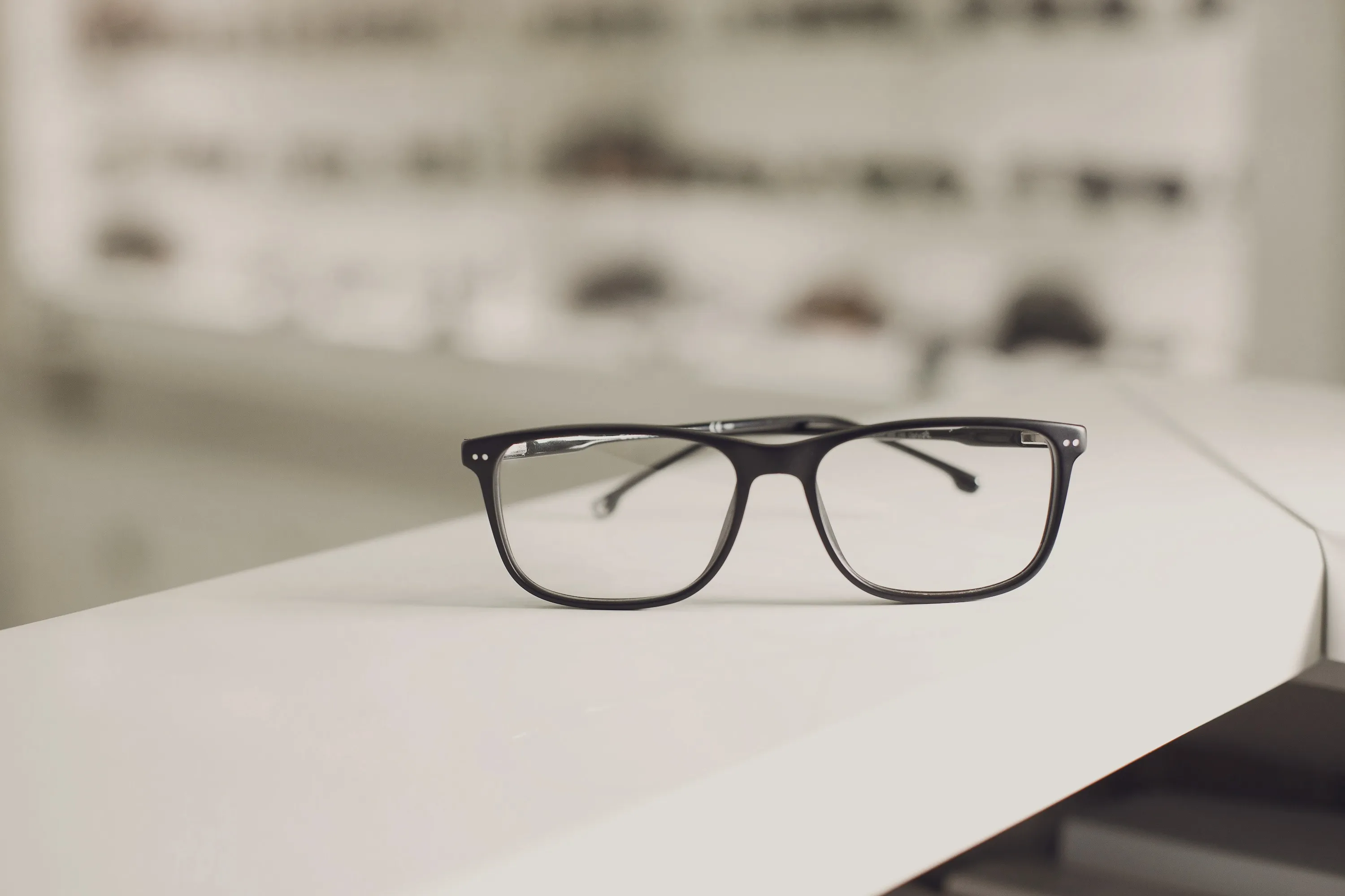 Black eyeglasses with rectangular frames resting on a white surface.