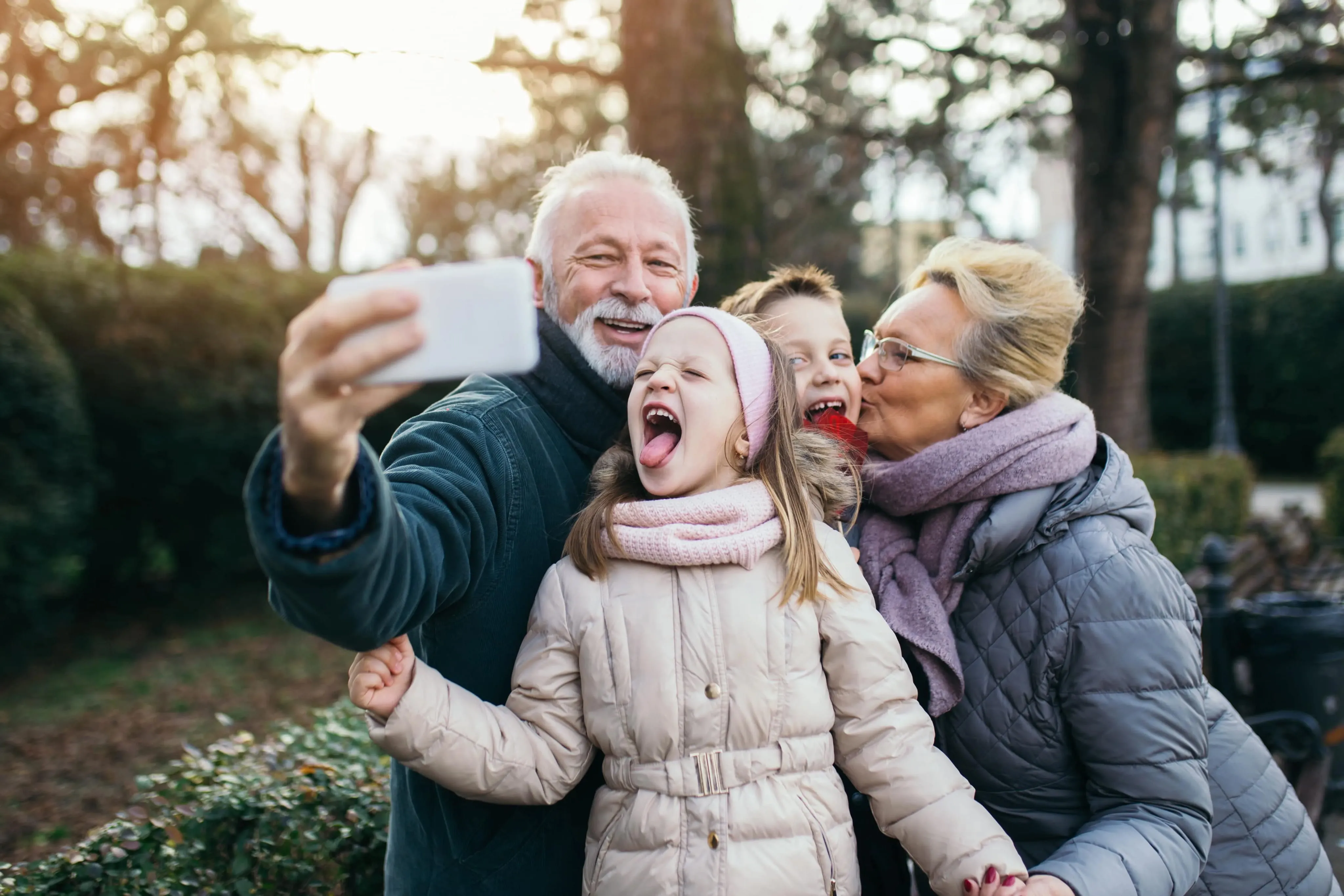 Elderly couple taking a selfie outside with two children, one child playfully sticking out their tongue.