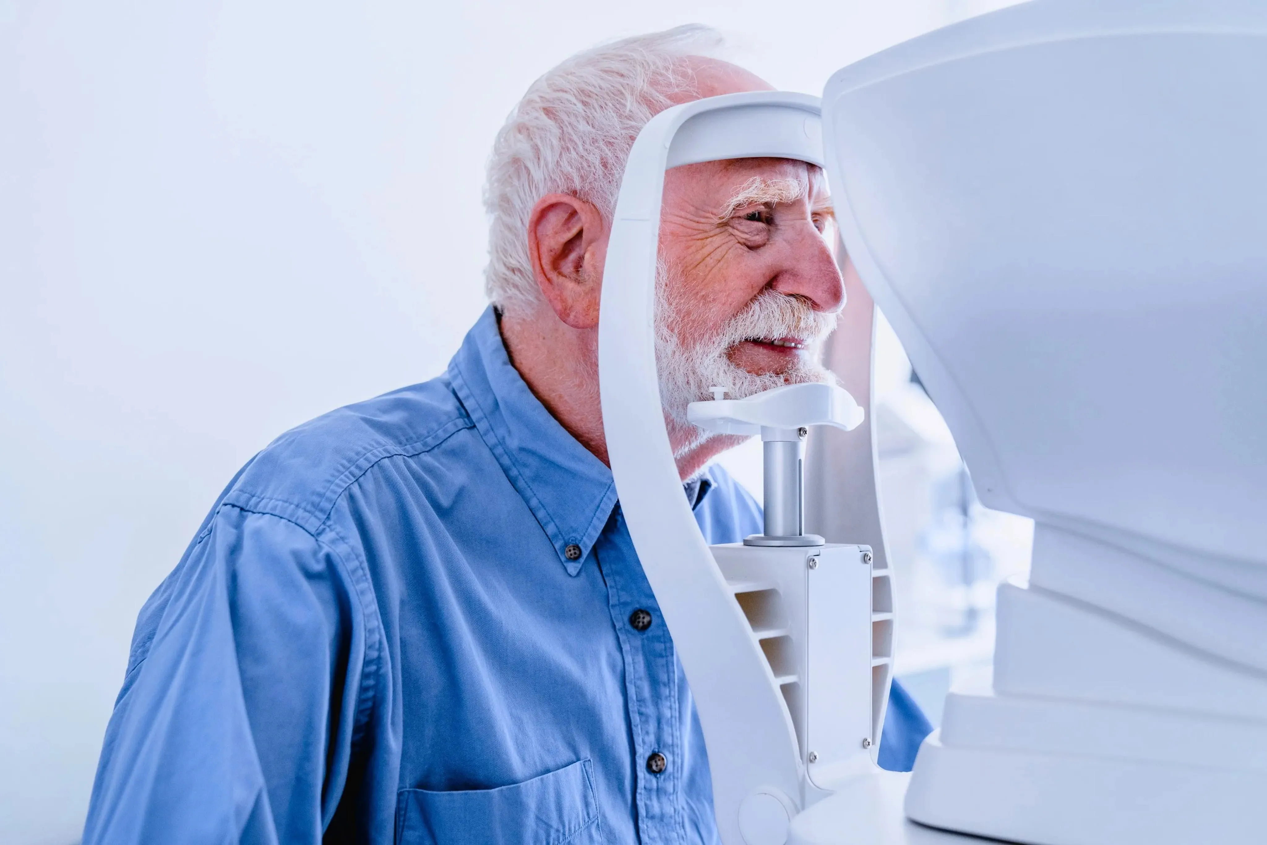 Elderly man in blue shirt undergoing an eye exam using an optical coherence tomography machine.