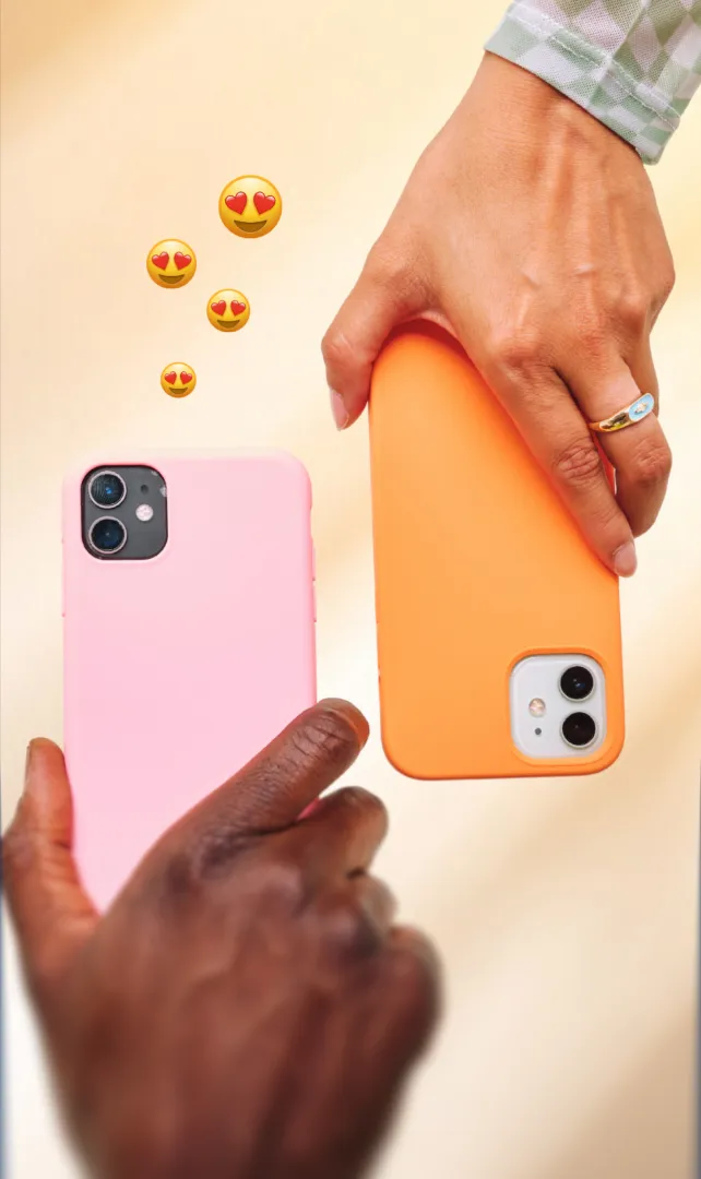 Two hands holding smartphones with pink and orange cases, heart emojis floating between them