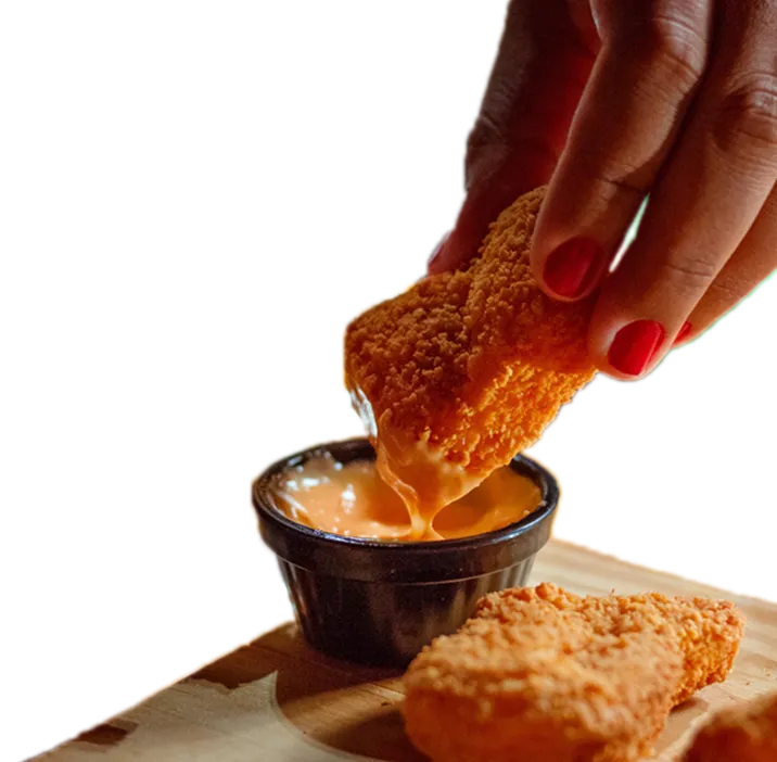 Hand dipping a breaded snack into a cup of cheese sauce