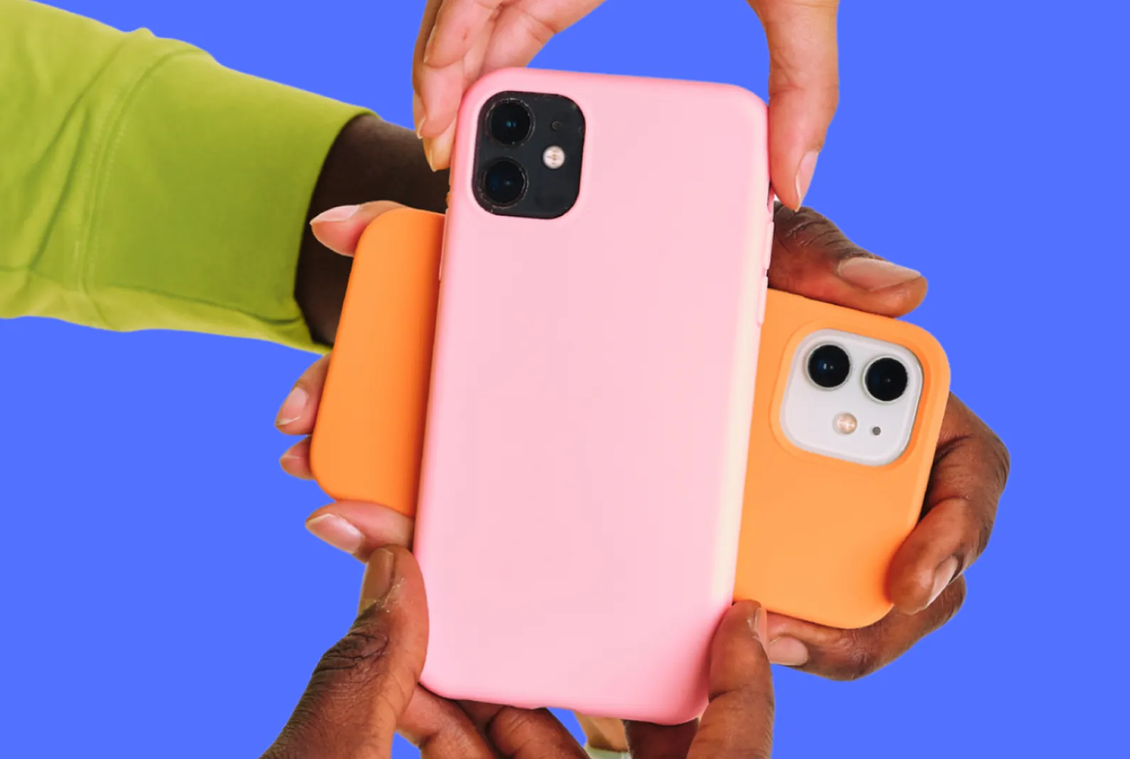 Hands holding multiple smartphones with pink and orange cases against a blue background