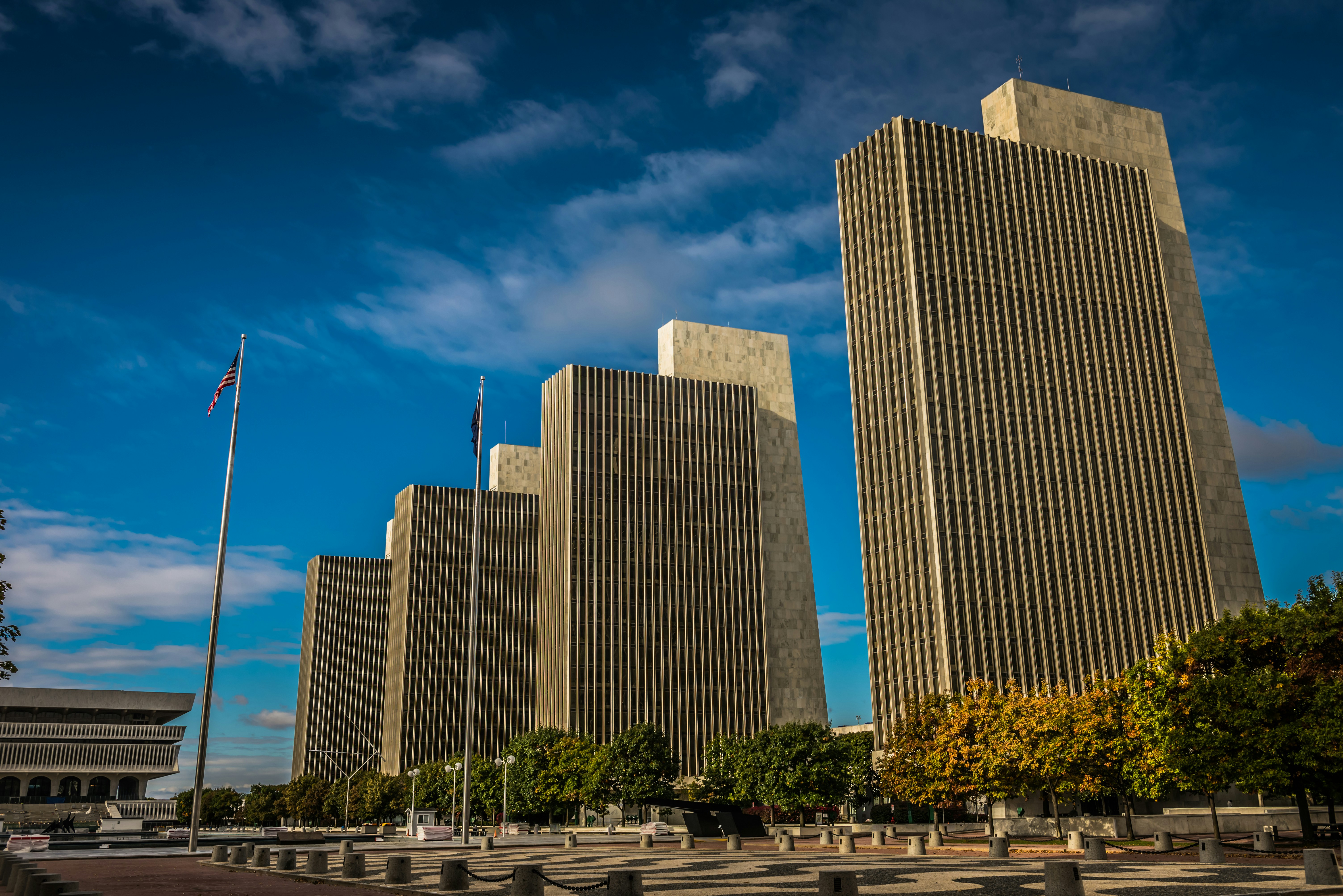 Four tall rectangular office buildings with vertical lines under a blue sky with scattered clouds.
