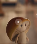 A small, whimsical clay figure with a hooded cloak and a rounded face with eyes, sitting on a surface.