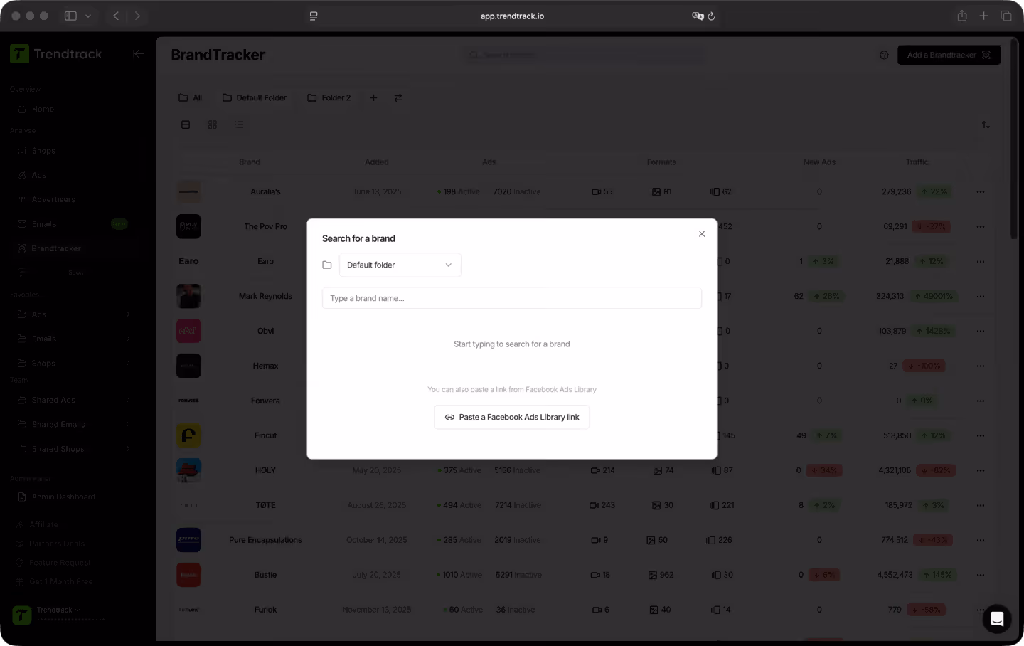 User interface of the Trendtrack BrandTracker showing a popup window for searching a brand with a folder dropdown, brand name input field, and an option to paste a Facebook Ads Library link.