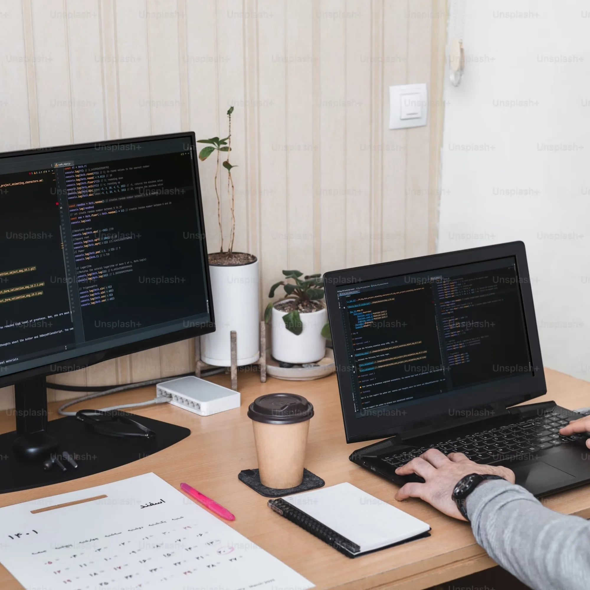 Een thuiwerkplek waar een laptop en een externe monitor staat. op het bureau staat een wegwerkbeker koffie en een kladblok. achter de laptop is iemand op het toetsenbord aan het typen