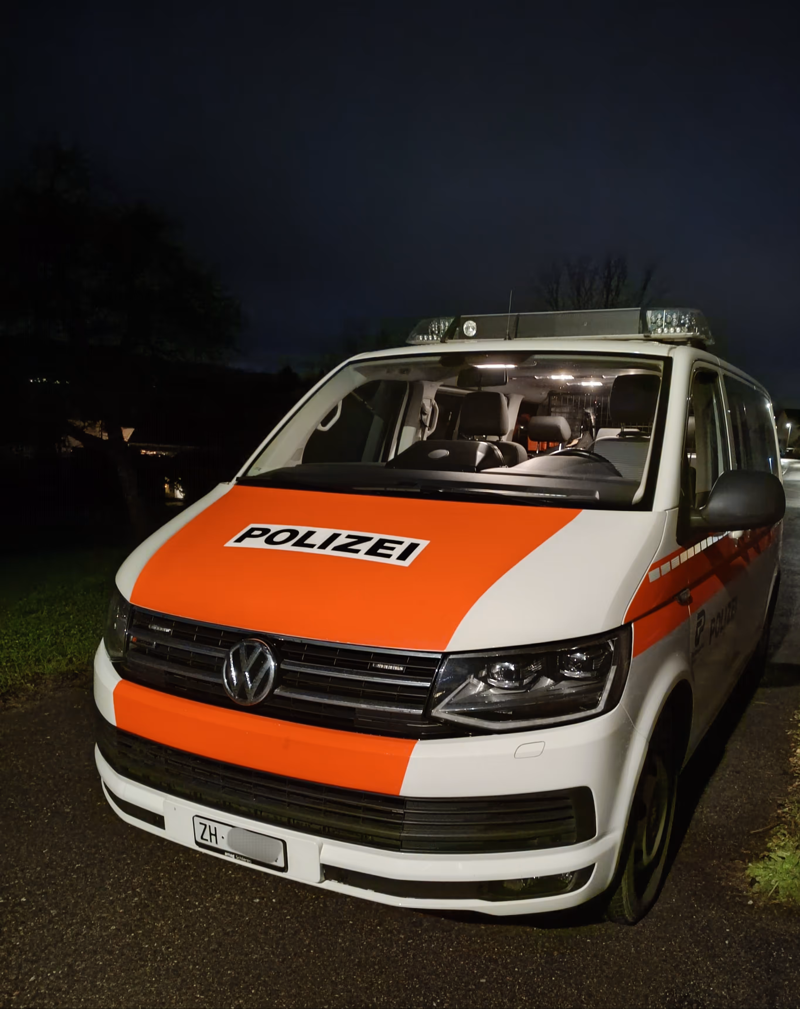Weisser und oranger Schweizer Polizeibus der Marke Volkswagen bei Nacht geparkt.
