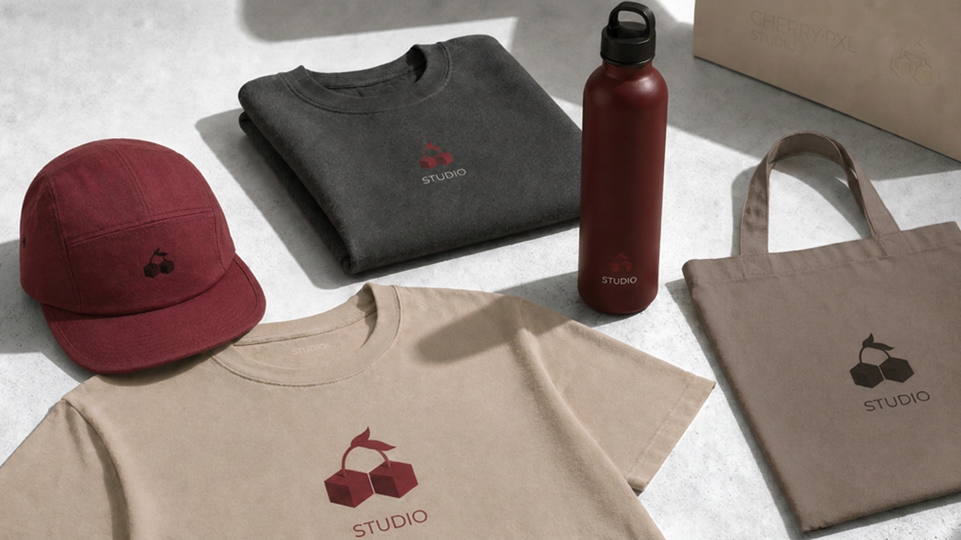 Collection merch Cherry PXL Studio posée à plat : casquette, sweatshirt, t-shirt, gourde, tote bag et packaging