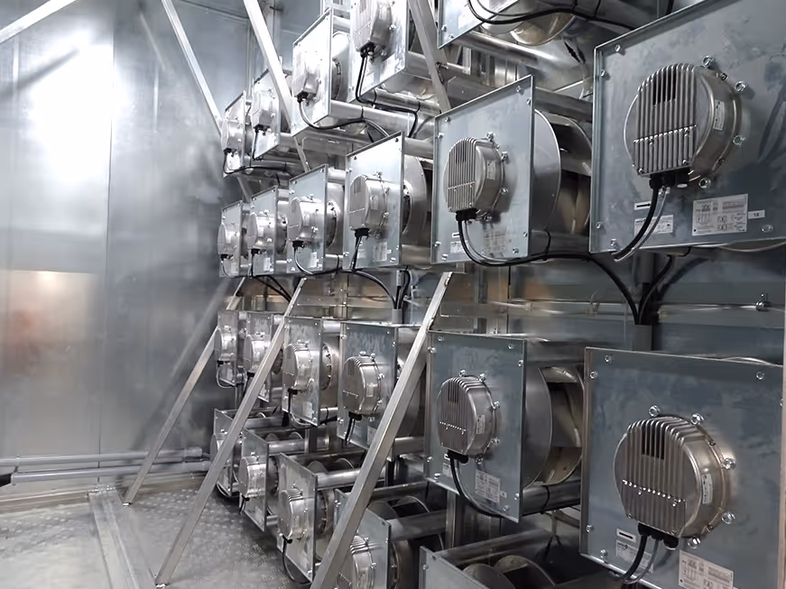 Rows of industrial metal ventilation fans mounted on a metallic wall inside a facility.