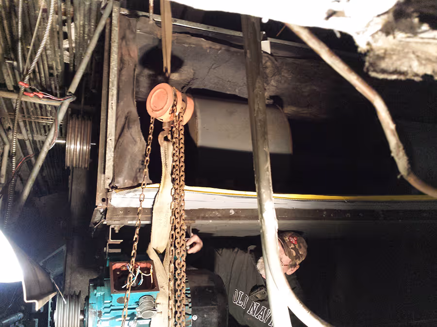 Man working with chains and mechanical equipment in a dimly lit industrial setting.
