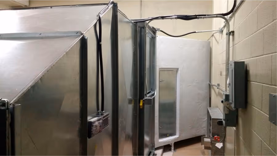 Metal HVAC ductwork and electrical panels installed in a narrow utility room with cinder block walls.