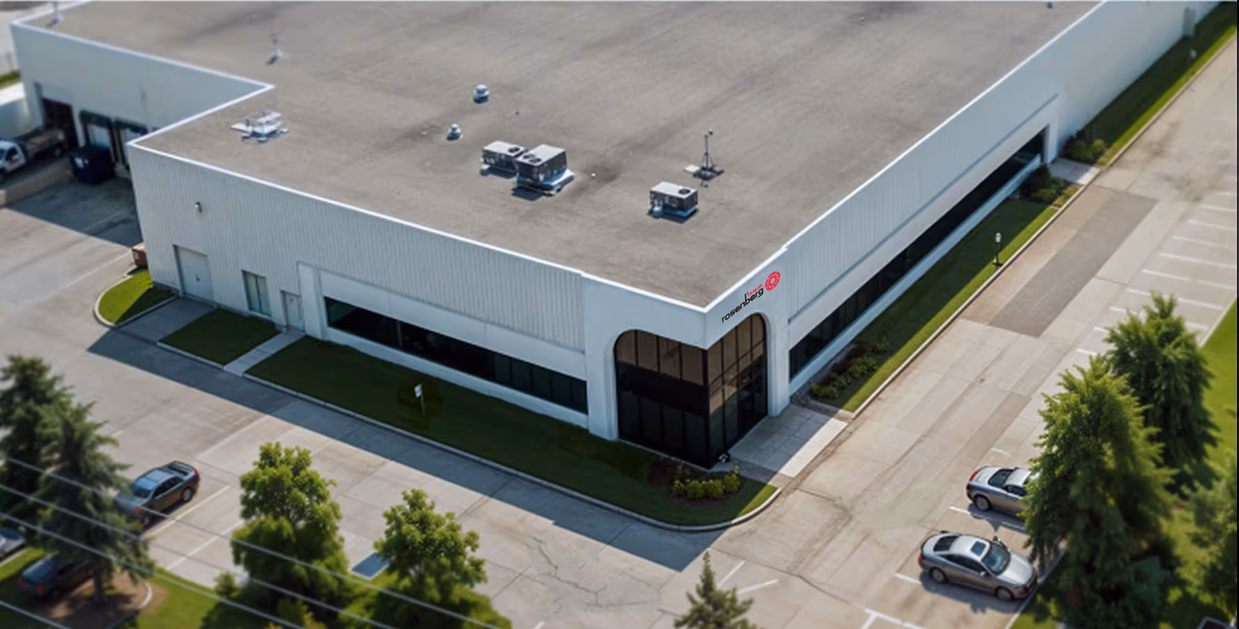Aerial view of a white commercial building with large windows, rooftop units, and adjacent parking.