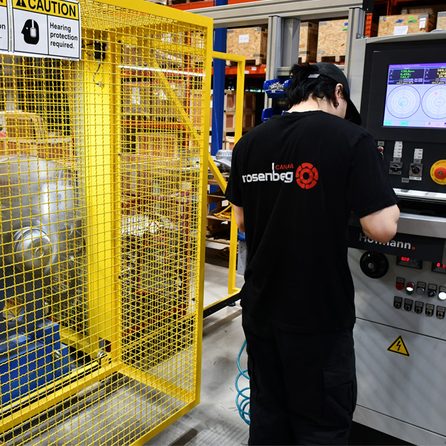Worker operates control panel next to yellow safety cage in industrial warehouse setting.