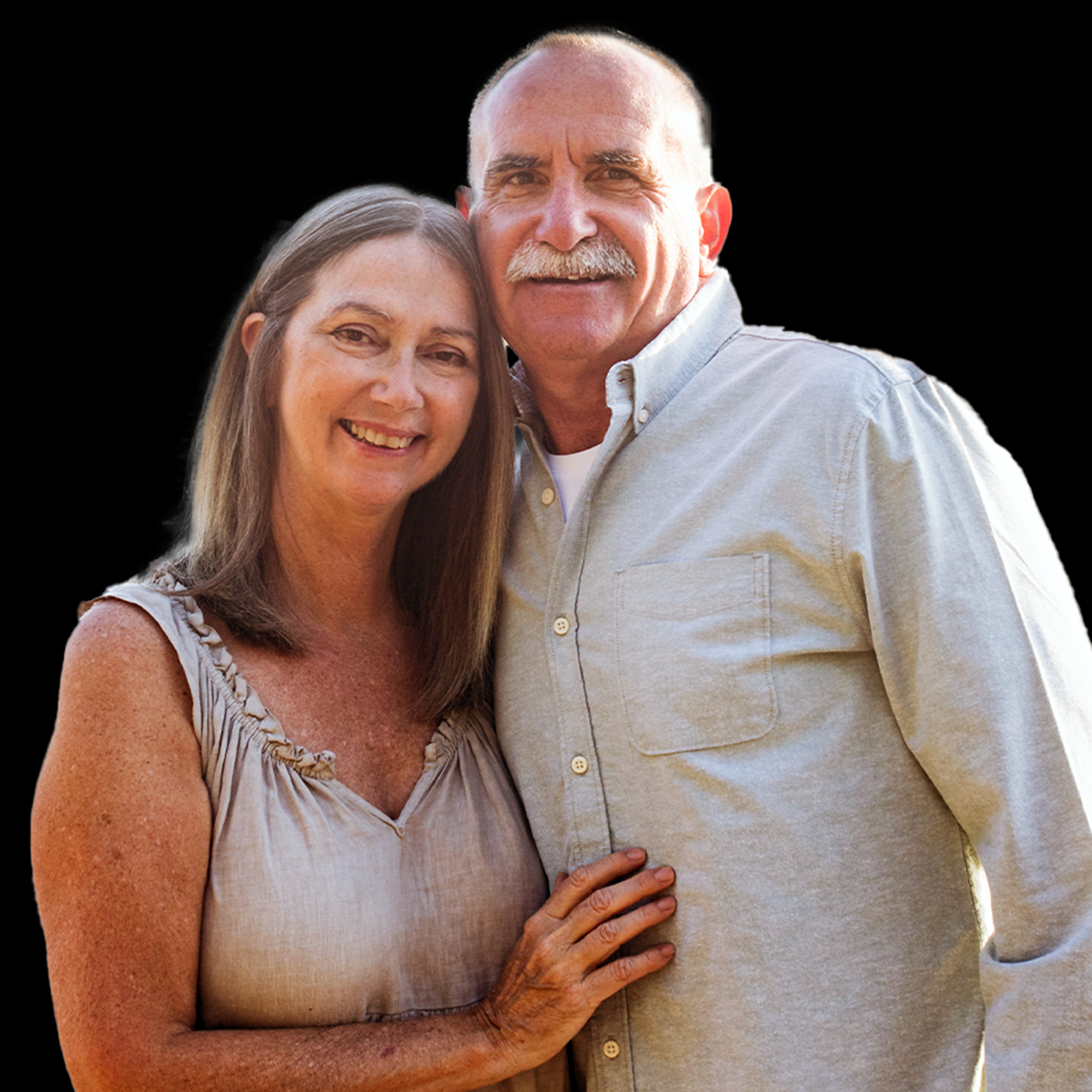 Smiling older couple standing close together, woman with brown hair wearing sleeveless top, man with mustache wearing light button-up shirt.