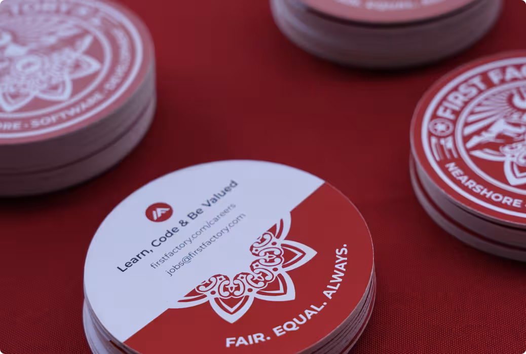 Round cards on a red surface with text 'Learn, Code & Be Valued' and email 'jobs@firstfactory.com' along with 'FAIR. EQUAL. ALWAYS.'