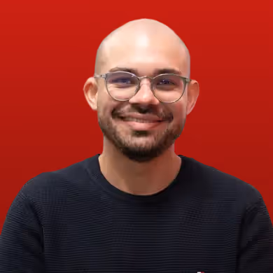 Smiling bald man with glasses and a dark sweater against a red background.